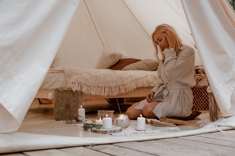 In einem Zelt sitzt eine junge Frau mit Kerzen auf dem Boden.