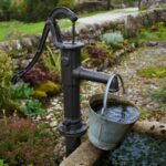 Alte Hand- Wasserpumpe befördert Wasser in einem Sammelbecken